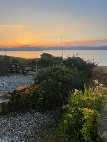 a sunset over the ocean with a fence and flowers at The Rowanberry Suite at Rowan Cottage in Elgol