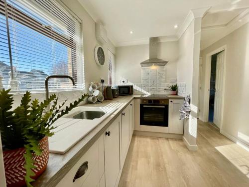 a white kitchen with a sink and a window at Charming 2 Bedroom Bungalow with open plan living in Felixstowe
