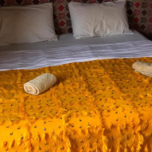a bed with an orange blanket and pillows on it at Erg Chegaga Camp & Activites in Mhamid