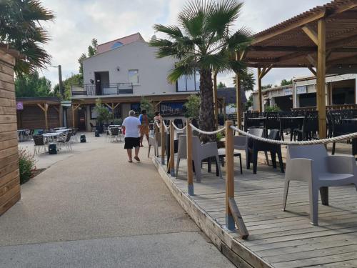 two people walking down a boardwalk with chairs and tables at Les sables du midi in Valras-Plage