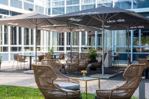 um pátio com cadeiras e mesas e um guarda-sol em Flightgate Munich Airport Hotel, a member of Radisson Individuals em Hallbergmoos