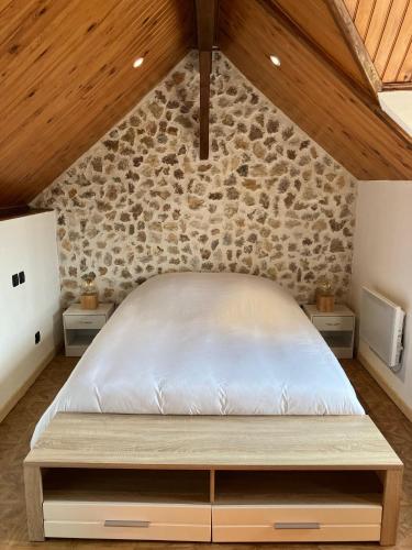 Cama en habitación con pared de piedra en La petite maison de la vallée, en Bazainville