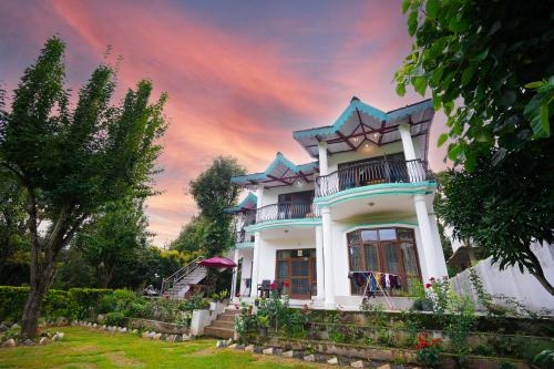 a large white house with a sunset in the background at Chirping Hills Resort,Bhimtal in Bhīm Tāl