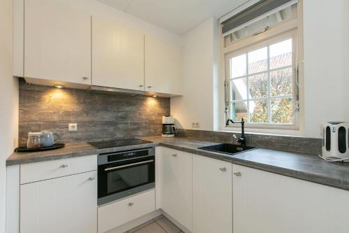 a kitchen with white cabinets and a sink and a window at Vakantiehuis Schanszicht in Lievelde