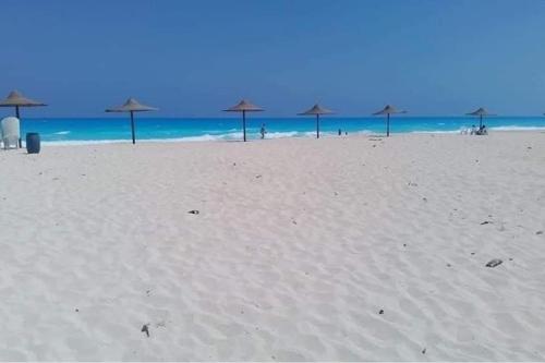 a group of umbrellas on a beach with the ocean at Cheerful fully furnished 3 bedroom villa in North Coast in Dawwār Abū Maḩrūs