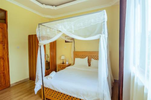 1 dormitorio con cama con dosel y sábanas blancas en Rayan Apartments & Safaris, en Arusha