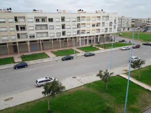 a street with cars parked in front of a large building at Appt à plage sidi Rahal in Sidi Rahal