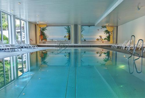 a large swimming pool with chairs and a large window at Modern renoviert mit Hallenbad + Fitness in Laax