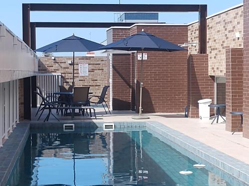 einen Pool mit Stühlen und Sonnenschirmen neben einem Backsteingebäude in der Unterkunft Apartamento em Ubatuba in Ubatuba