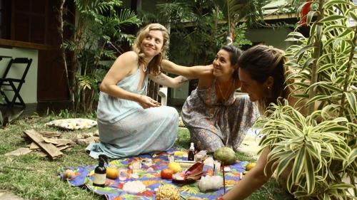 three women sitting on the grass with a picnic blanket at POUSADA ENCANTO DO AMOR in Búzios
