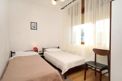 a bedroom with two beds and a chair and a window at Apartments by the sea Ugljan - 830 in Ugljan