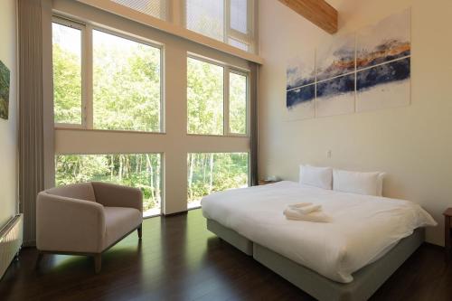 a bedroom with a bed and a chair and windows at Annupuri Onsen Chalet in Niseko