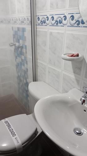 a white bathroom with a toilet and a sink at HOTEL GALERAS in Pasto