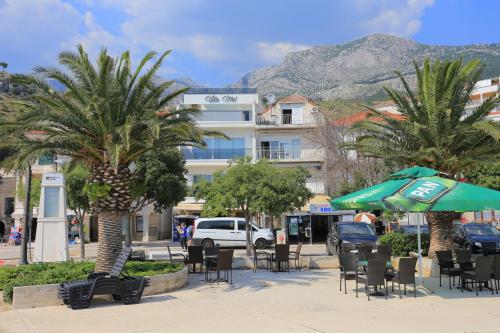 a hotel with tables and chairs and palm trees at Apartments by the sea Podgora, Makarska - 18918 in Podgora