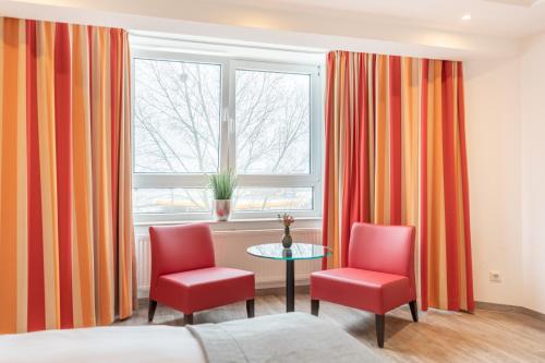 a room with two red chairs and a table and a window at Select Hotel A1 Bremen-Stuhr in Stuhr