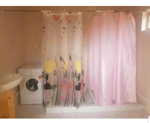 a bathroom with a washing machine and a pink shower curtain at Guest house Umar in Tong