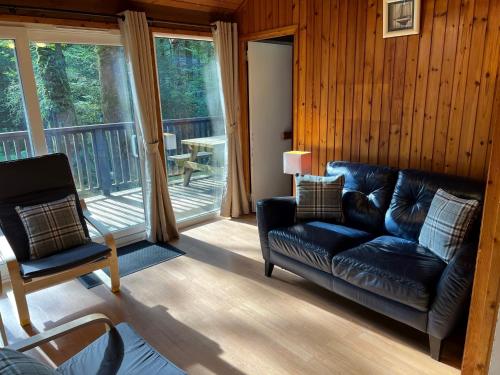 a living room with a leather couch and a balcony at Loch Aweside Forest Cabins in Dalavich