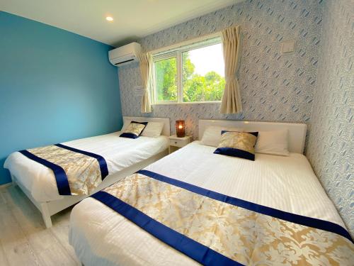 2 camas en una habitación con paredes azules y ventana en グランディオーソ沖縄プールヴィラ恩納6 en Onna
