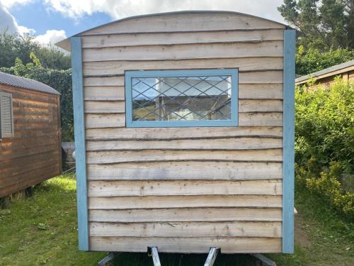 a wooden outhouse with a window in a yard at Modern Shepherd's Hut at St Anne's in Plymouth