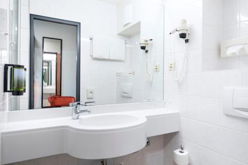 een witte badkamer met een wastafel en een spiegel bij ACHAT Hotel Monheim am Rhein in Monheim
