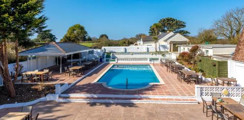 uma piscina com mesas e cadeiras num pátio em Saints Bay Hotel em St Martin Guernsey