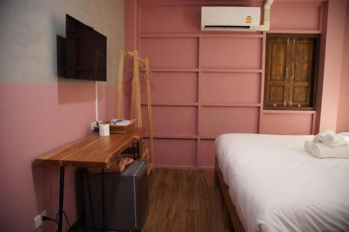 um quarto com paredes cor-de-rosa, uma cama e uma secretária. em Tali-Yailai Hostel em Pattaya Central