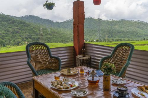 a table and chairs on a balcony with a view at Zostel Homes Harabhag, Jogindernagar in Bīr