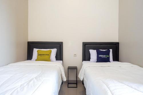 2 letti con lenzuola bianche e cuscini gialli e blu di Urbanview Hotel Syariah John Sweet Home by RedDoorz a Tegal