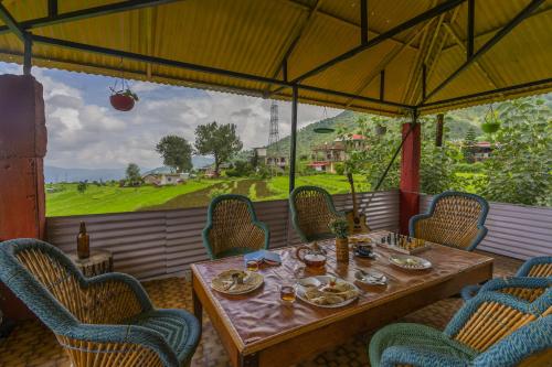 a table and chairs on a patio with a view at Zostel Homes Harabhag, Jogindernagar in Bīr