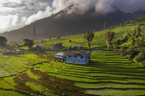 a village in the middle of a field with a mountain at Zostel Homes Harabhag, Jogindernagar in Bīr