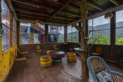 a room with a table and chairs and windows at Zostel Homes Harabhag, Jogindernagar in Bīr