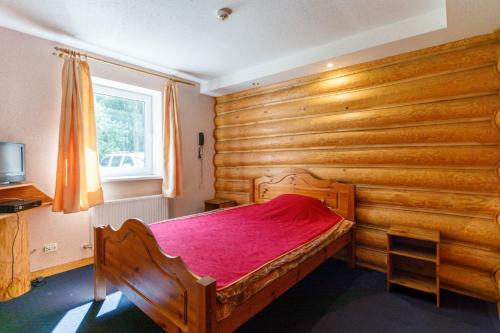 a bedroom with wooden walls and a wooden bed with red sheets at Viesu nams “Dimantu ferma” in Ikšķile