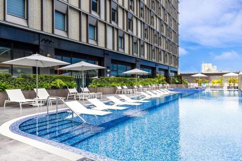 uma piscina do hotel com cadeiras brancas e guarda-sóis em Hotel Collective em Naha