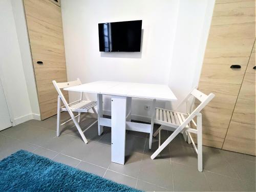 una mesa y sillas blancas con TV en la pared en Les Halles Appartements, en París