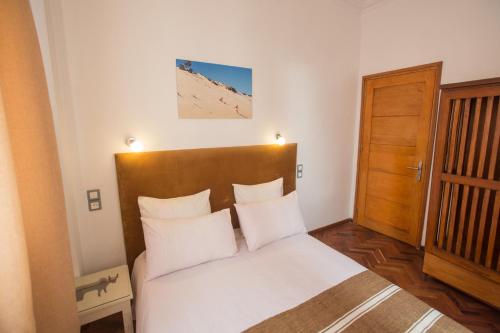- une chambre avec un lit doté de draps blancs et d'une porte en bois dans l'établissement Hasambarana Apparthotel, à Antananarivo
