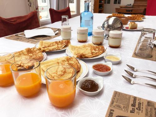una mesa con platos de comida y vasos de zumo de naranja en Normand'Histoire Chambres d'Hôtes en Isigny-sur-Mer
