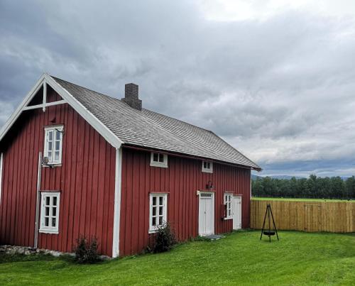 un granero rojo en un campo con una valla en Tranøya en Tranøya