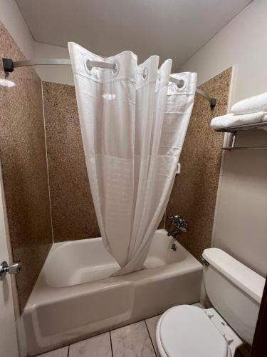 a bathroom with a tub and a toilet with a shower curtain at Days Inn by Wyndham Daytona Beach Speedway in Daytona Beach
