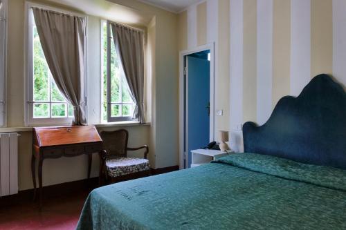 a bedroom with a bed and a desk and windows at Hotel Club i Pini - Residenza d'Epoca in Versilia in Lido di Camaiore