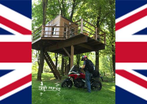 un homme debout à côté d'une moto devant une cabane dans les arbres dans l'établissement Medže Dirbtuve, 