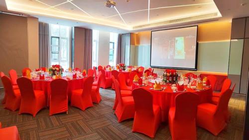 a conference room with red tables and chairs and a screen at Holiday Inn Shanghai Dishui Lake by IHG in Nanhui