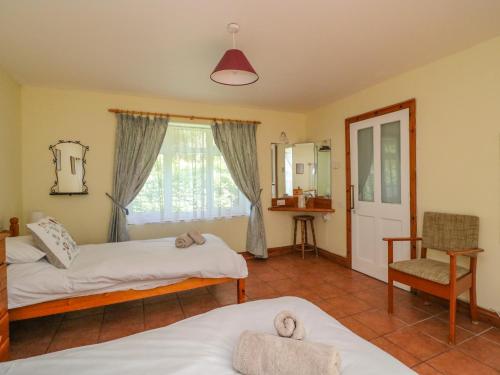 a bedroom with two beds and a window and a chair at Mimosa Cottage in Swyre