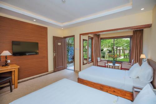 a bedroom with two beds and a desk and a television at Celina Peninsula Resort Quảng Bình in Dương Cảnh