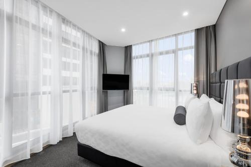 a bedroom with a white bed and large windows at Meriton Suites Church Street, Parramatta in Sydney
