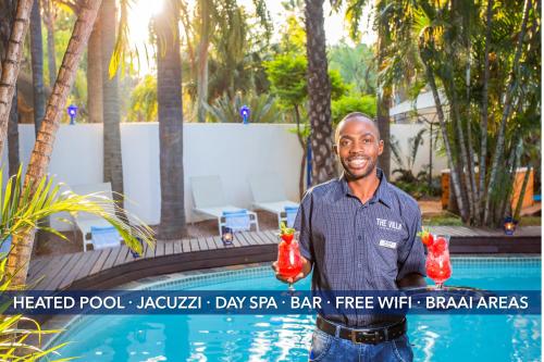 a man standing next to a pool holding two drinks at The Villa Manor & Spa in Bela-Bela