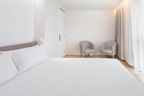 a white bedroom with two chairs and a bed at B&B HOTEL Santo Tirso in Santo Tirso