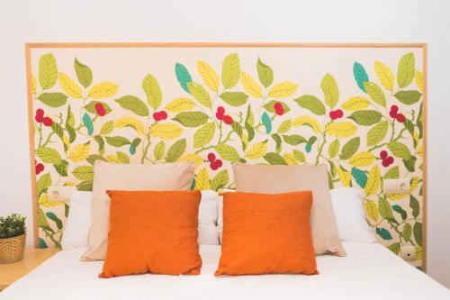 Bett mit orangefarbenen Kissen vor einer floralen Wand in der Unterkunft Céntrico Apartamento en Calle Carreteria - Malaga in Málaga