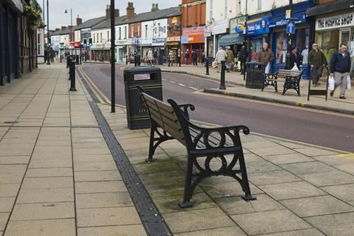 un banc sur un trottoir dans une rue de la ville dans l'établissement Private Room wigan, à Atherton