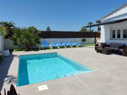 a swimming pool in a yard with chairs and a house at VILLA SANCTI PETRI in Chiclana de la Frontera