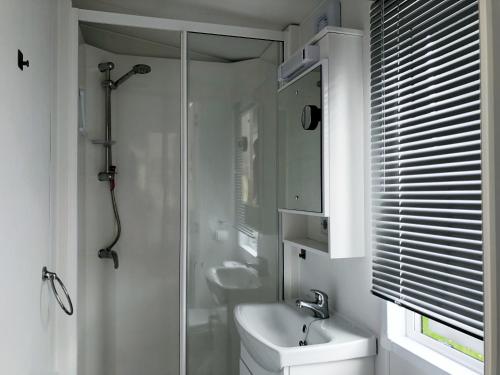a white bathroom with a shower and a sink at Chalet 516 op Recreatiepark De Wielen in Sint Maarten